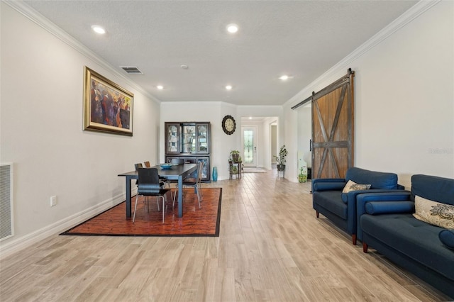 living area featuring light wood-style flooring, a textured ceiling, a barn door, crown molding, and baseboards