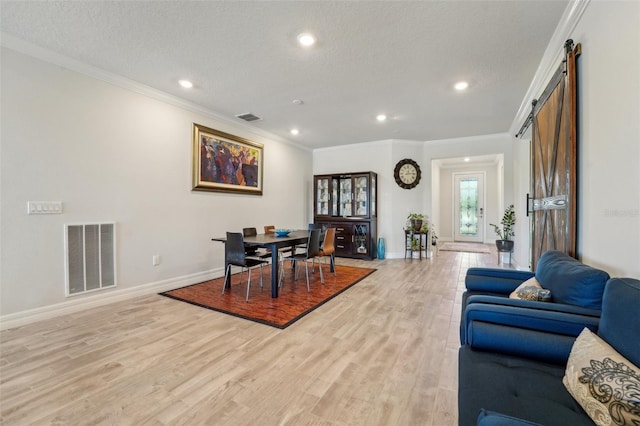 dining area with visible vents, a barn door, light wood-style flooring, and crown molding