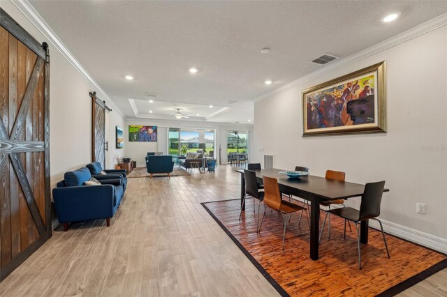 dining room with a barn door, visible vents, light wood-style flooring, and ornamental molding