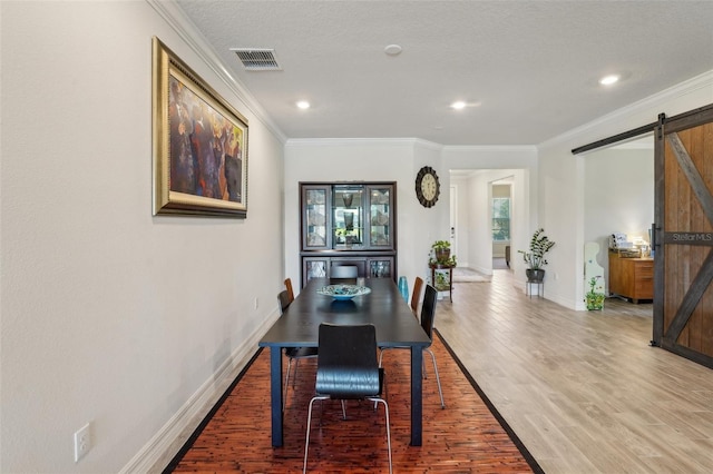 dining area featuring a barn door, visible vents, wood finished floors, and ornamental molding