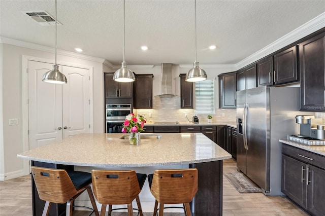 kitchen with wall chimney range hood, a breakfast bar area, visible vents, and appliances with stainless steel finishes