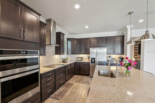 kitchen with light stone countertops, a sink, dark brown cabinetry, appliances with stainless steel finishes, and wall chimney exhaust hood