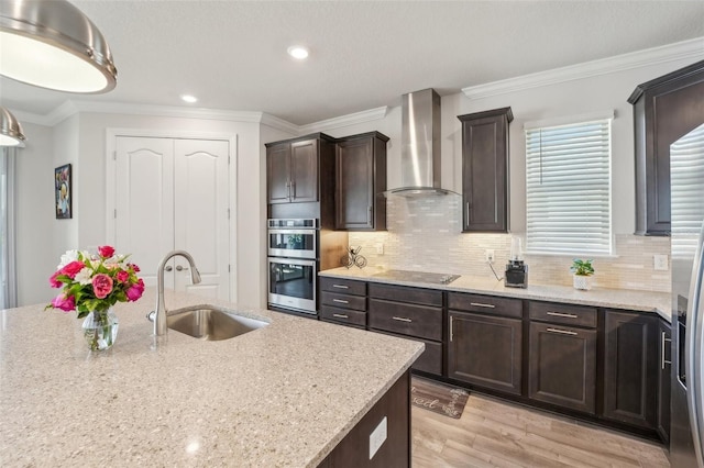 kitchen featuring black electric stovetop, a sink, crown molding, double oven, and wall chimney range hood