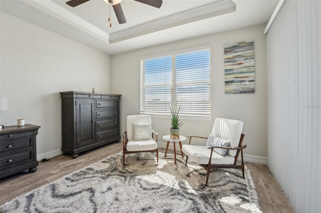 living area with light wood-type flooring, a tray ceiling, baseboards, and crown molding