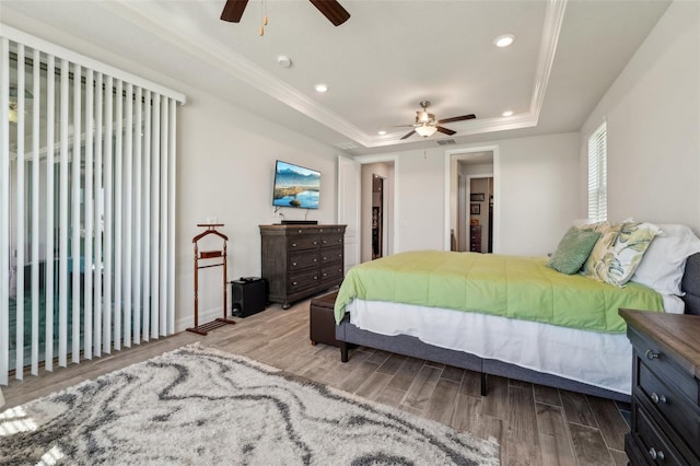 bedroom featuring a ceiling fan, a raised ceiling, wood finished floors, and ornamental molding