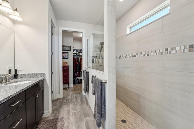 bathroom featuring a walk in closet, wood finished floors, baseboards, walk in shower, and vanity