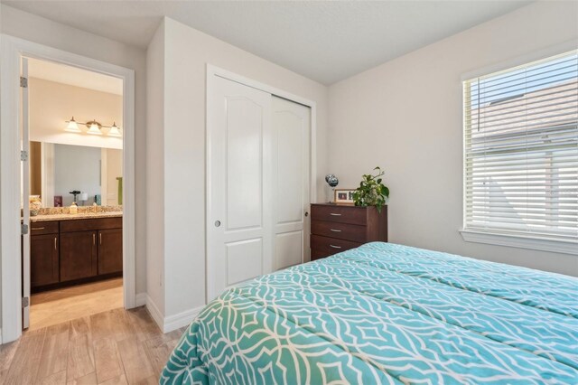 bedroom featuring a closet, baseboards, ensuite bath, and light wood-style flooring