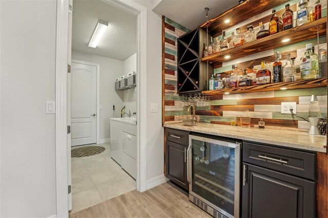 bar featuring beverage cooler, backsplash, a textured ceiling, separate washer and dryer, and wet bar