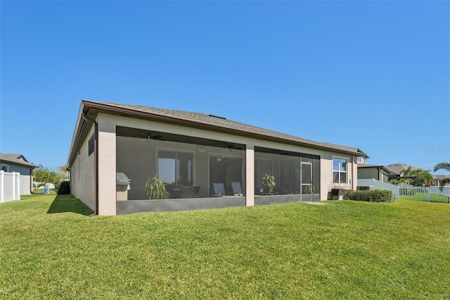 rear view of property featuring stucco siding, a sunroom, a yard, and fence