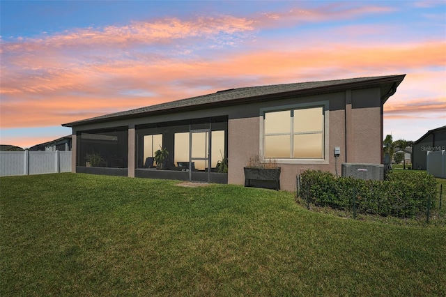 back of house at dusk with a yard, a sunroom, fence, and stucco siding