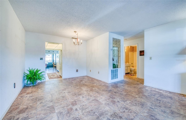 spare room with a textured ceiling, visible vents, and a chandelier