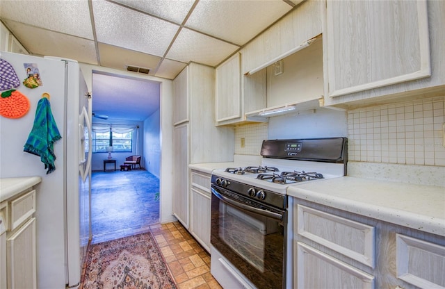 kitchen featuring visible vents, a drop ceiling, freestanding refrigerator, light countertops, and gas range oven