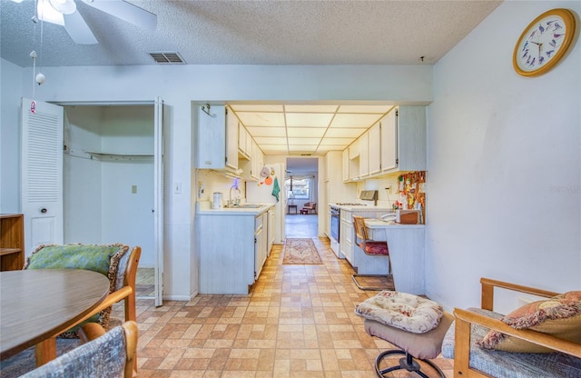 kitchen with a ceiling fan, visible vents, white range with gas stovetop, a sink, and light countertops