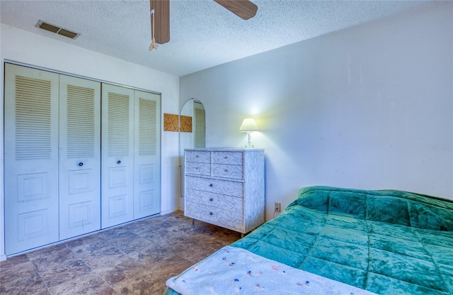 bedroom featuring a closet, visible vents, a textured ceiling, and a ceiling fan