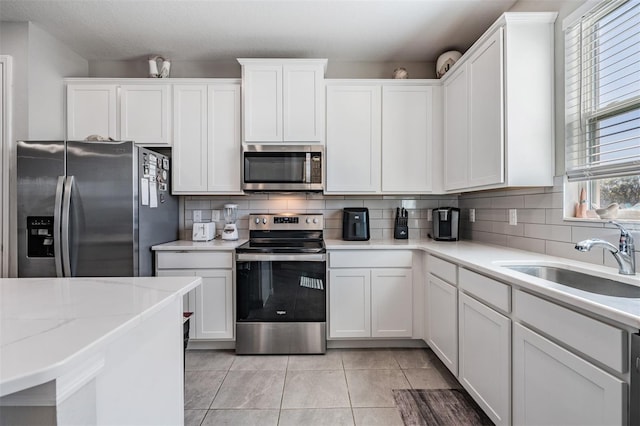 kitchen with light tile patterned floors, a sink, white cabinets, appliances with stainless steel finishes, and tasteful backsplash