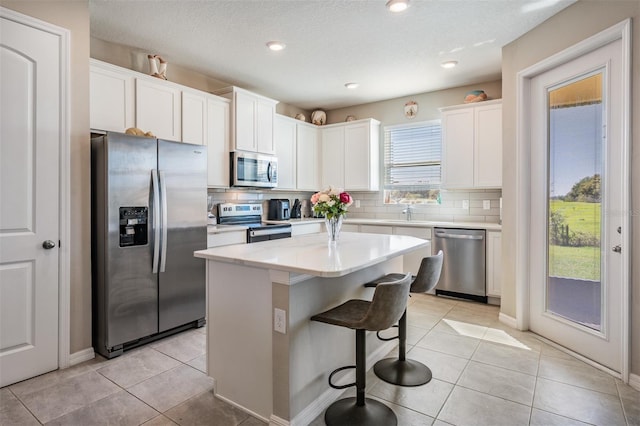 kitchen with light tile patterned flooring, backsplash, appliances with stainless steel finishes, and a kitchen island