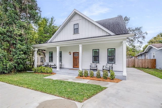 modern inspired farmhouse with a front lawn, fence, covered porch, board and batten siding, and a shingled roof