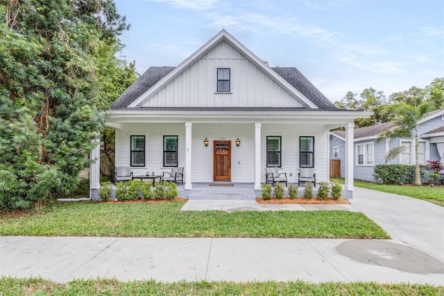 modern inspired farmhouse with covered porch, board and batten siding, a front yard, and roof with shingles