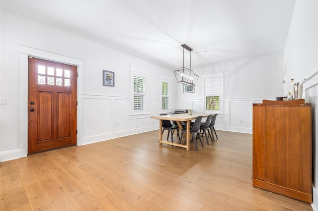 dining area with a decorative wall, a notable chandelier, wainscoting, and light wood-type flooring