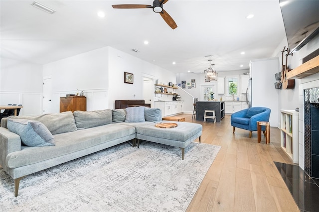 living room with visible vents, a fireplace with flush hearth, recessed lighting, light wood-style flooring, and ceiling fan with notable chandelier