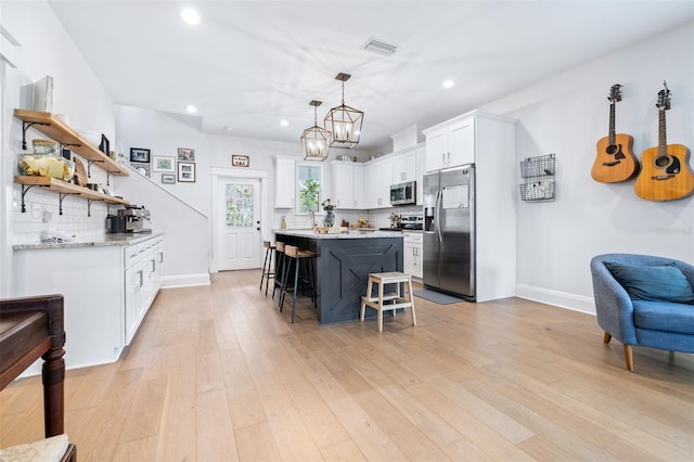 kitchen with a kitchen bar, visible vents, white cabinetry, stainless steel appliances, and light wood finished floors