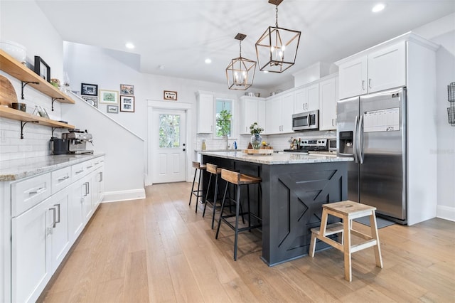 kitchen with light wood finished floors, white cabinets, a kitchen breakfast bar, and stainless steel appliances