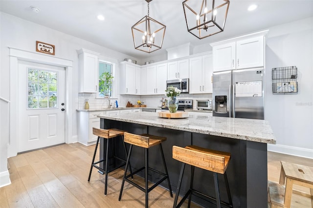 kitchen with light wood-style flooring, a center island, white cabinetry, appliances with stainless steel finishes, and decorative backsplash