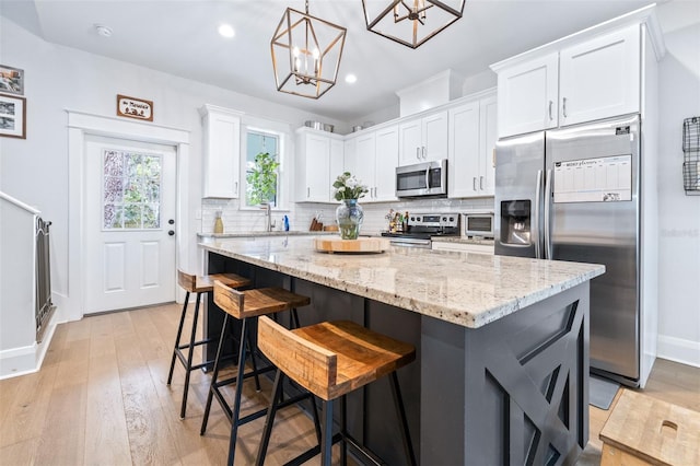 kitchen featuring tasteful backsplash, a center island, white cabinetry, stainless steel appliances, and light stone countertops