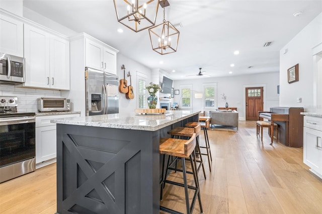 kitchen with stainless steel appliances, light wood-style floors, white cabinetry, a kitchen breakfast bar, and backsplash