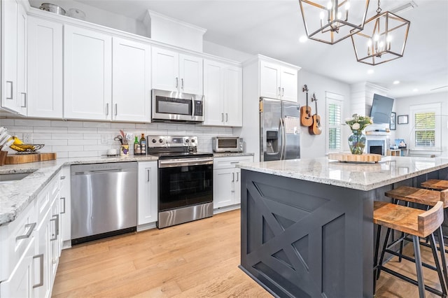 kitchen featuring a kitchen bar, backsplash, white cabinetry, stainless steel appliances, and light wood finished floors