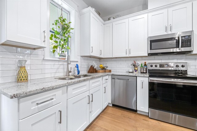 kitchen with a sink, decorative backsplash, light wood-style floors, appliances with stainless steel finishes, and white cabinetry