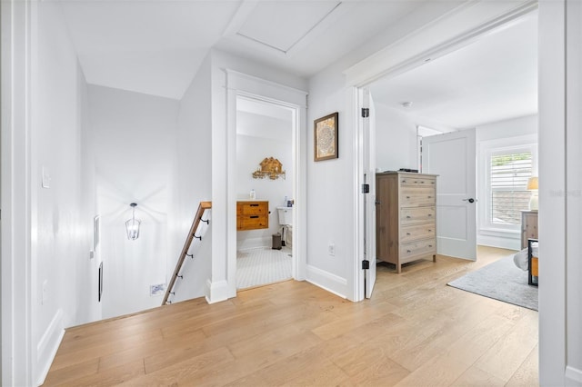 hall with an upstairs landing, attic access, baseboards, and light wood-style floors