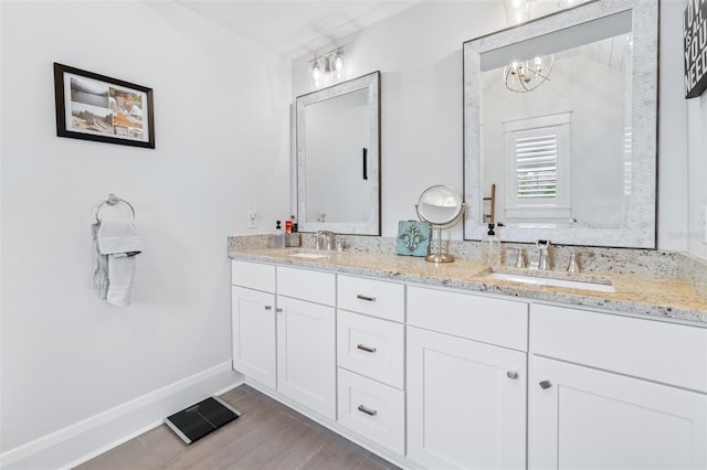 full bath featuring double vanity, wood finished floors, baseboards, and a sink