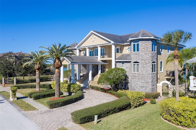 exterior space featuring stone siding, stucco siding, decorative driveway, and a balcony