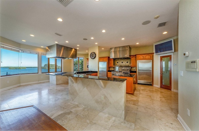 kitchen featuring visible vents, a spacious island, extractor fan, dark countertops, and stainless steel fridge