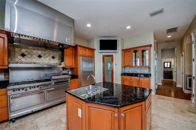 kitchen with wall chimney range hood, high end appliances, visible vents, and a sink