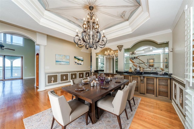 dining room with arched walkways, crown molding, a raised ceiling, and light wood-style floors