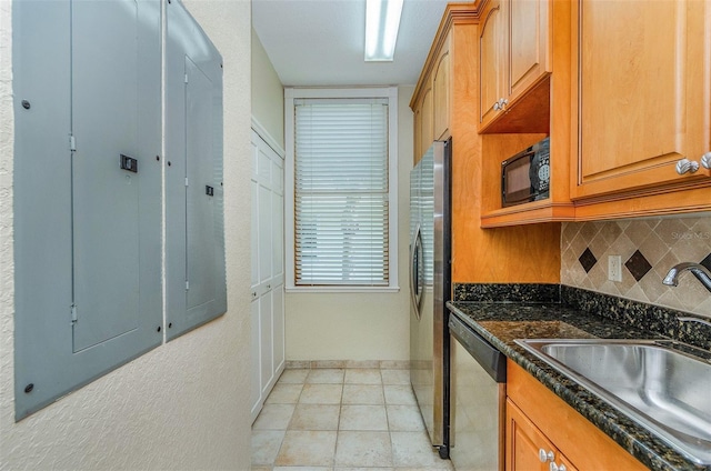 kitchen featuring dark stone countertops, electric panel, a sink, stainless steel appliances, and tasteful backsplash