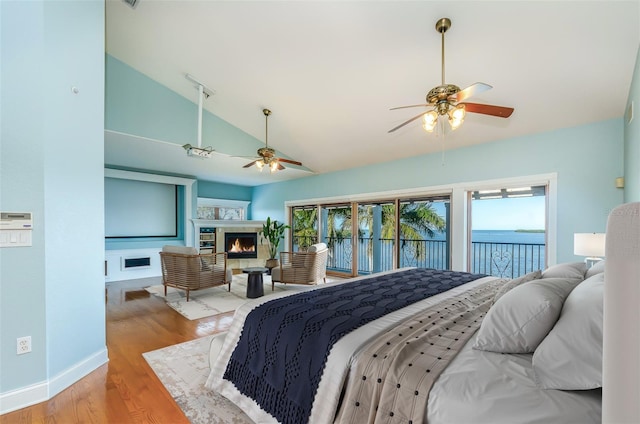 bedroom featuring baseboards, lofted ceiling, a lit fireplace, wood finished floors, and access to outside