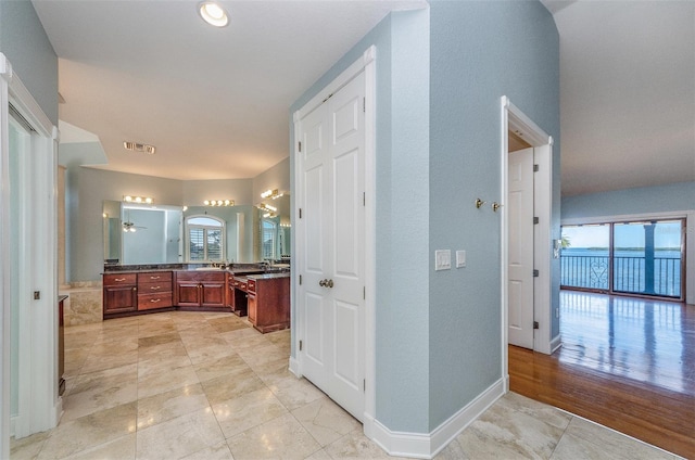 hallway with a wealth of natural light, visible vents, baseboards, and a sink