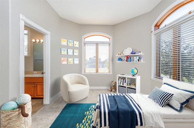 bedroom featuring a sink, light colored carpet, baseboards, and connected bathroom