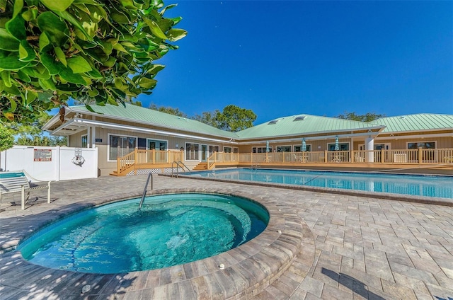 pool with a wooden deck, a patio, a community hot tub, and fence