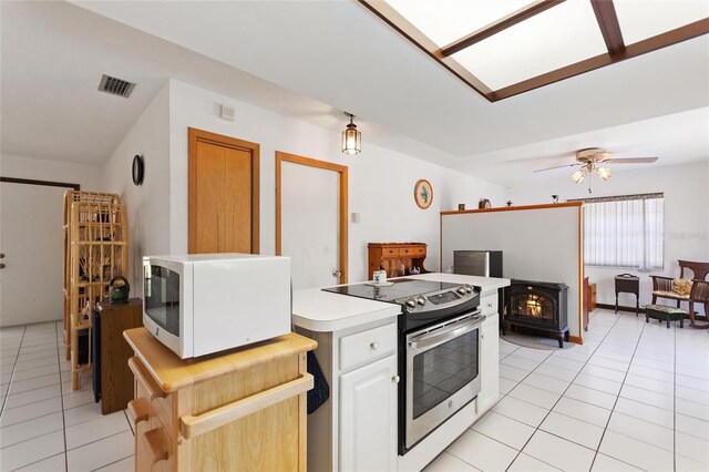 kitchen featuring light tile patterned floors, white microwave, stainless steel range with electric stovetop, and a wood stove