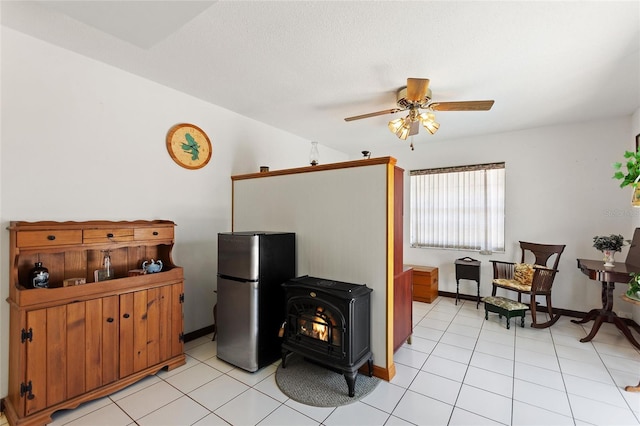 kitchen with a wood stove, light tile patterned flooring, freestanding refrigerator, and ceiling fan