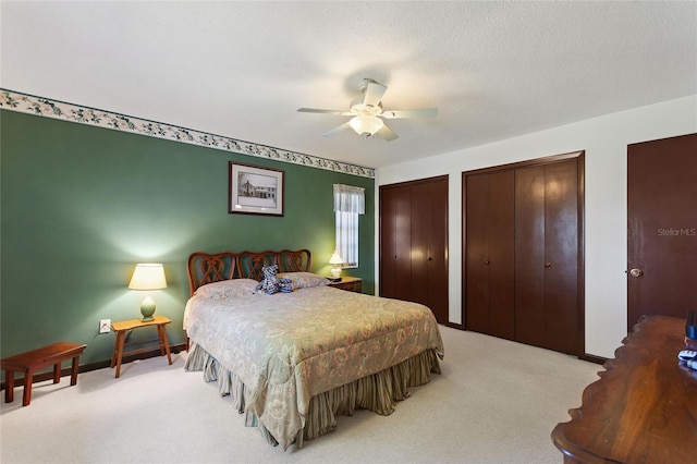 bedroom with ceiling fan, baseboards, multiple closets, light carpet, and a textured ceiling