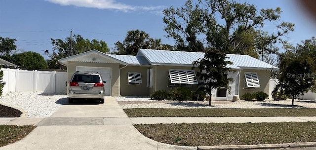 ranch-style home featuring metal roof, an attached garage, driveway, and fence