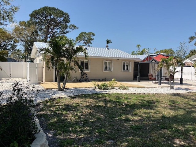 back of property featuring fence, a wooden deck, metal roof, a yard, and a patio