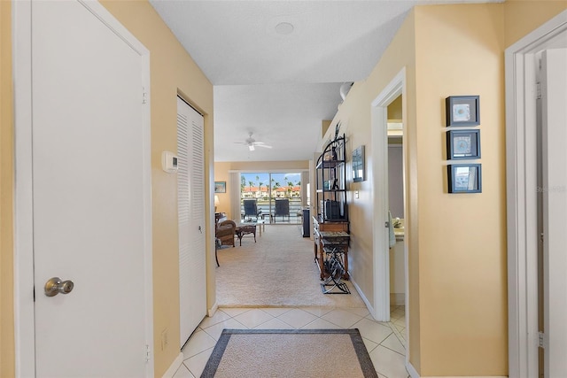 corridor featuring light tile patterned floors, baseboards, and light carpet