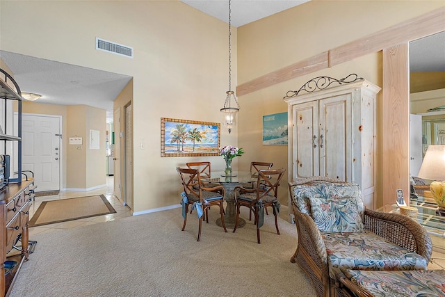 dining space featuring visible vents, baseboards, light colored carpet, a high ceiling, and light tile patterned flooring