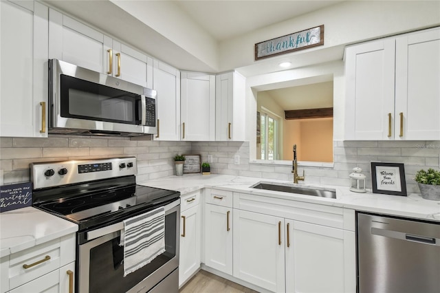 kitchen with a sink, stainless steel appliances, tasteful backsplash, and white cabinetry